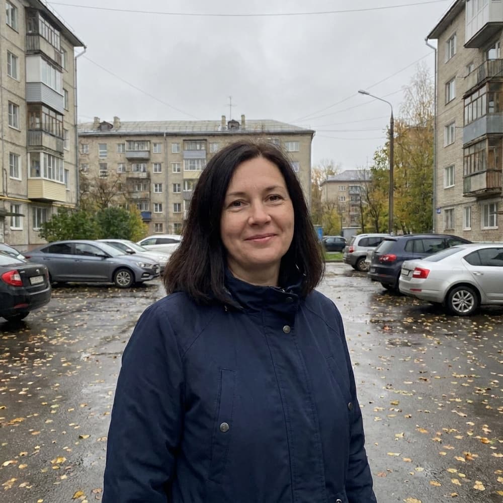 Обычный снимок с телефона: женщина в тёмно-синей куртке стоит во дворе жилых домов пасмурным осенним днём